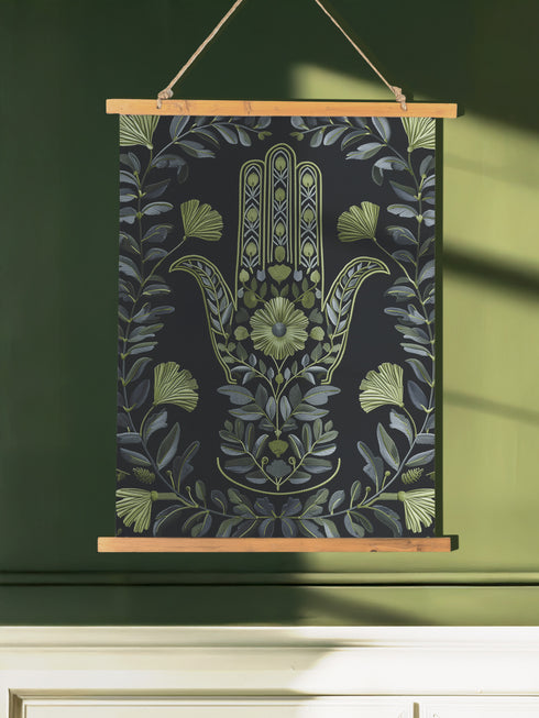 Botanical Hamsa wall tapestry featuring intricate sage green and lavender design on black background, showing a protective hand symbol surrounded by leaf motifs and floral elements, hanging from wooden dowels with natural twine.
